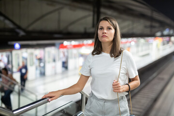 Young modern woman moving on subway station escalator