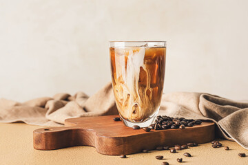 Board with glass of cold brew and coffee beans on color table against light background