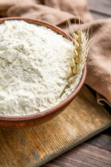 Bowl with flour and wheat ear on dark wooden background, closeup