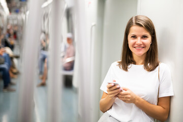 Fototapeta na wymiar Smiling girl using smartphone in subway wagon