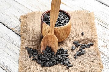 Fototapeta na wymiar Bowl and spoon of black sunflower seeds on white wooden background