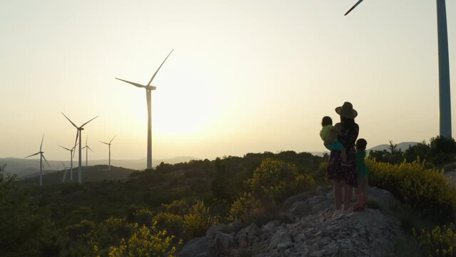 Aerial view mother with children stands and shows them the windmills that produce electricity. Sources of ecological and clean energy, nature conservation and laughter together in the mountains.