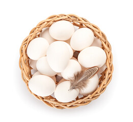 Wicker basket with chicken eggs and feather on white background