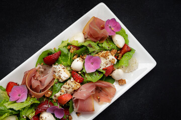 Salad with prosciutto, strawberries and mozzarella, on a dark