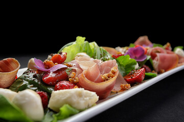 Salad with prosciutto, strawberries and mozzarella, on a dark