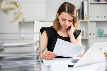 Portrait of woman office worker sitting at table and doing her daily paperwork.