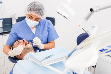 Female dentist in face mask with male patient during checkup at dental clinic office