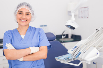 Obraz premium Portrait of a positive young female dentist in uniform with crossed hands at the dental office