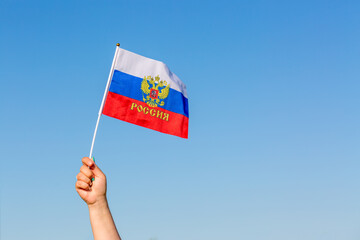 Female hand holding flag of Russia against blue sky