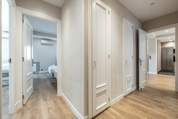 hallway of a house with white woodwork and light wood floors with access to several rooms