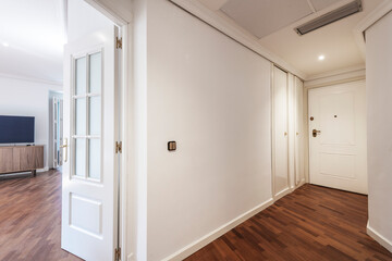 Entrance hall and corridor of a house with dark parquet floors, plain white painted walls and white...