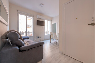 Entrance hall and corridor of a house with light wood parquet flooring, large balconies with wooden doors and metal railings and a sofa in the foreground
