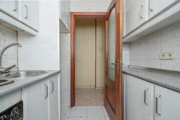 Small kitchen with white cabinets on both sides, built-in appliances, gray wooden countertop and...