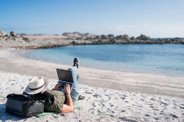 digital nomad lying on the beach outdoors alone working relaxed.
