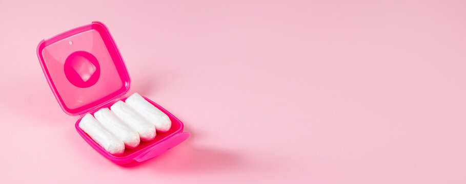 Tampons in pink box. Feminine hygiene products on pastel background. Menstruation and womens health concept. Banner format.