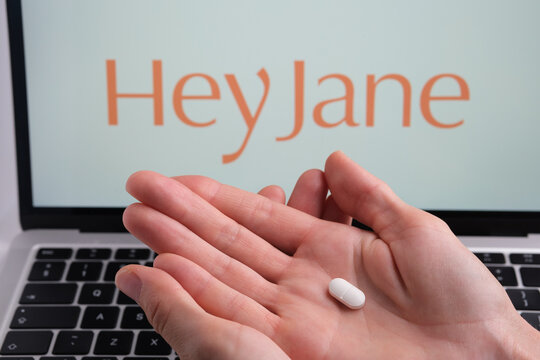 White pill in womans hand and Hey Jane company logo on a blurred background. Concept for online telehealth abortion platform. Stafford, United Kingdom, July 3, 2022