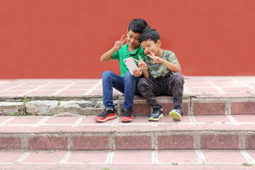 Fototapeta na wymiar Two dark-haired Latino children who are brothers or friends who live in poverty play video games with a cell phone, make video calls and take selfies 