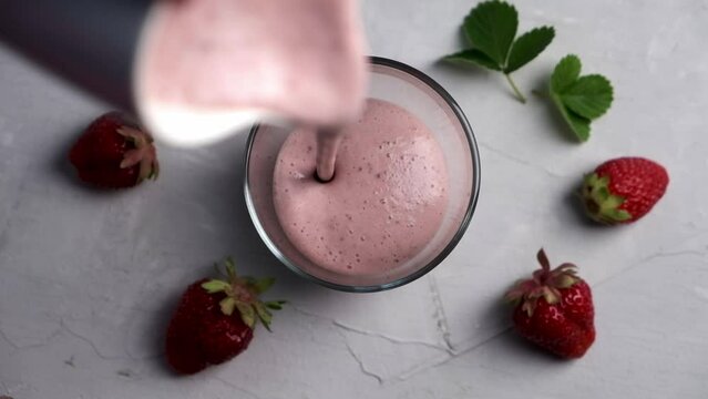 Pouring strawberry smoothie with protein into glass.
