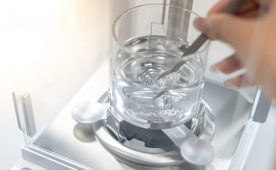Female hands use tweezertor calibrate the specific gravity precious stone to separate the type of stone with the Hydrostatic Weighing Balance.