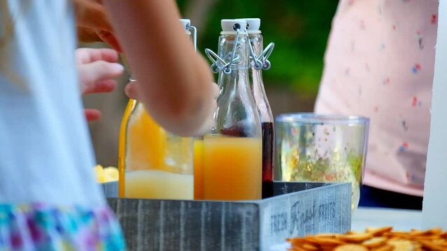 Childrens summer party.summer drink. Fruit juices and smoothies in glass bottles set.Children open and pour fruit drinks into glasses in a summer sunny garden.Slow motion.Friends in the summer garden