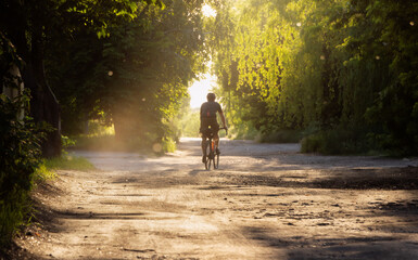 Cyclist rides bicycle on a gravel road at sunset. Soft focus.