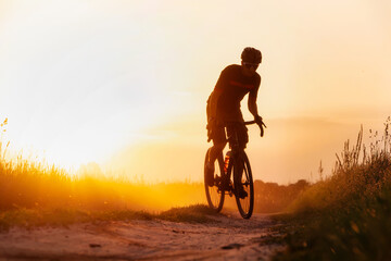 Fototapeta na wymiar Silhouette young of cyclist on a gravel bike riding on a dust trail at sunset.