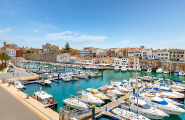 Fototapeta na wymiar The old port harbor of the historic city of Ciutadella de Menorca, Spain, with fishing boats in the marina and the shops and cafes in view under the walled medieval city.