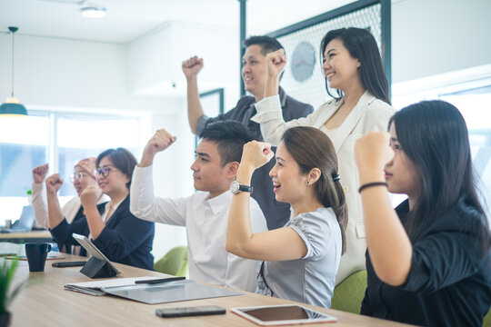Group of happy Asian business people smiling and holding fists up in celebration. Side view.