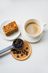 coffee beans in a black spoon with white coffee cup and toffee cake