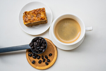 coffee beans in a black spoon with white coffee cup and toffee cake