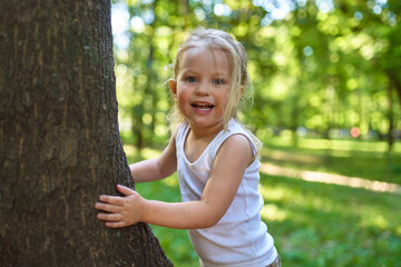 a child in the woods shows positive emotions standing next to a large tree