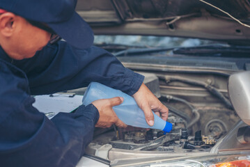 Car Mechanic man hands pouring Deionized purified Distilled water for car battery mechanical service. Close up hands man hold Deionized Distilled liquid water bottle at garage auto mobile car service