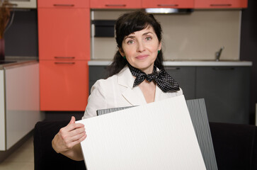 The woman shows samples of coatings for the kitchen set to choose the combination of colors - white and embossed grey.