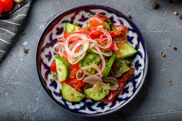 Vegetable salad with tomatoes and cucumbers with red onion on grey table top view, shakarop salad