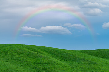 Naklejka premium rainbow over green field, blue sky in background