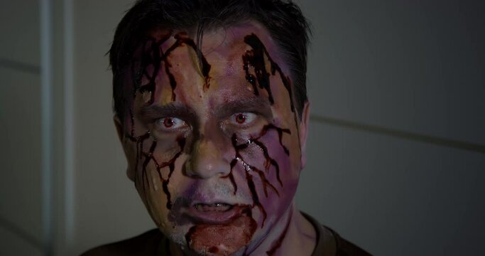 Portrait of man with braces on teeth who has just turned into a zombie. Undead with a bloody face and eyes clacks his teeth and growls, he is hungry, so he looks out for a prey
