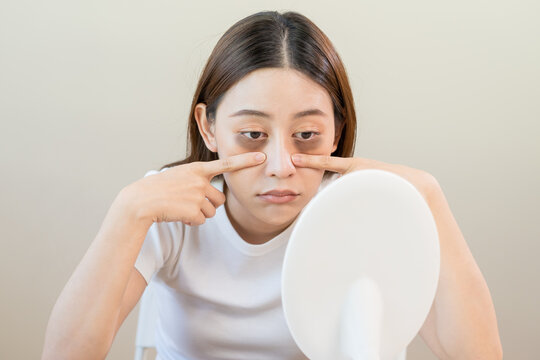 Bored, insomnia asian young woman, girl looking at mirror, without makeup, touch under eyes with problem of dark circles, puffiness, swollen or wrinkles on face. Sleepless, sleepy people, copy space