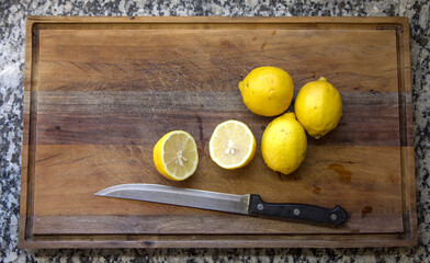 Overhead view of several whole and sliced ​​yellow lemons on a wooden board and a large knife