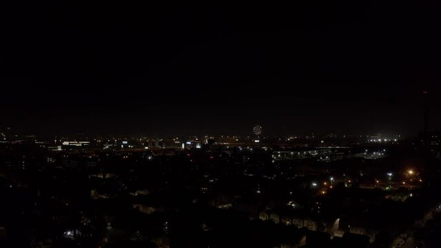 Red flares are set off from a Chicago residential area as large explosions appear on the horizon on a clear Independence day night. Drone lifting night shot