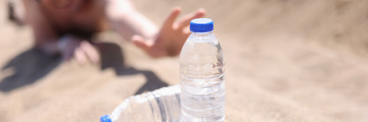 A man in the desert stretches on the sand for bottles of water