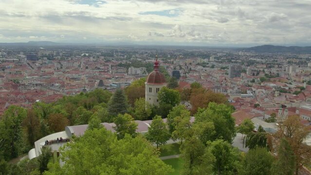 Aerial orbit view flying around landmark Glokenturm tower on Graz's Schlo&szlig;berg hilltop woodland park