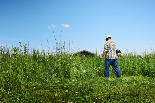 A man mows the grass in the field with a trimmer. Yard care concept. Front view.