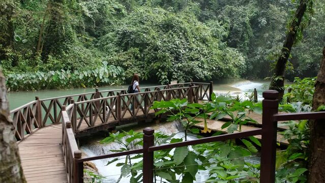 A female traveler and a dog walking on a red bridge by The Tat Kuang Si waterfall in Luang Prabang, Laos