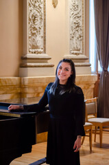 mujer latina mexicana cantante mezzosoprano  posando sonriente junto a un piano, vestido negro....