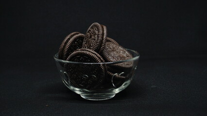A bowl of Cookies isolated on black background. Chocolate cookies with white cream filling on white bowl