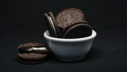 A bowl of Cookies isolated on black background. Chocolate cookies with white cream filling on white bowl