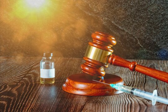 Judges hammer, syringe and vaccine bottle on a wooden background with sun light. Concept for a medical judgment