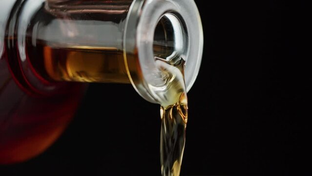 Pouring brandy or whiskey close-up. Luxury cognac on black background. Alcohol amber drink, drinking rum, liqour beverage in glass.