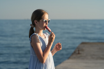 a beautiful Caucasian girl in a summer dress and sunglasses eats ice cream