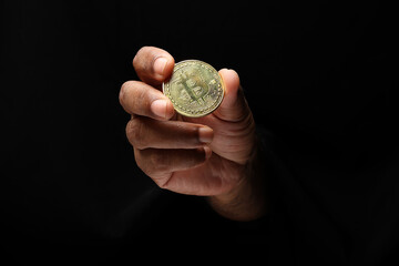 Asian male dark skinned single hand fist finger on black background holding golden fake sample physical bitcoin cryptocurrency